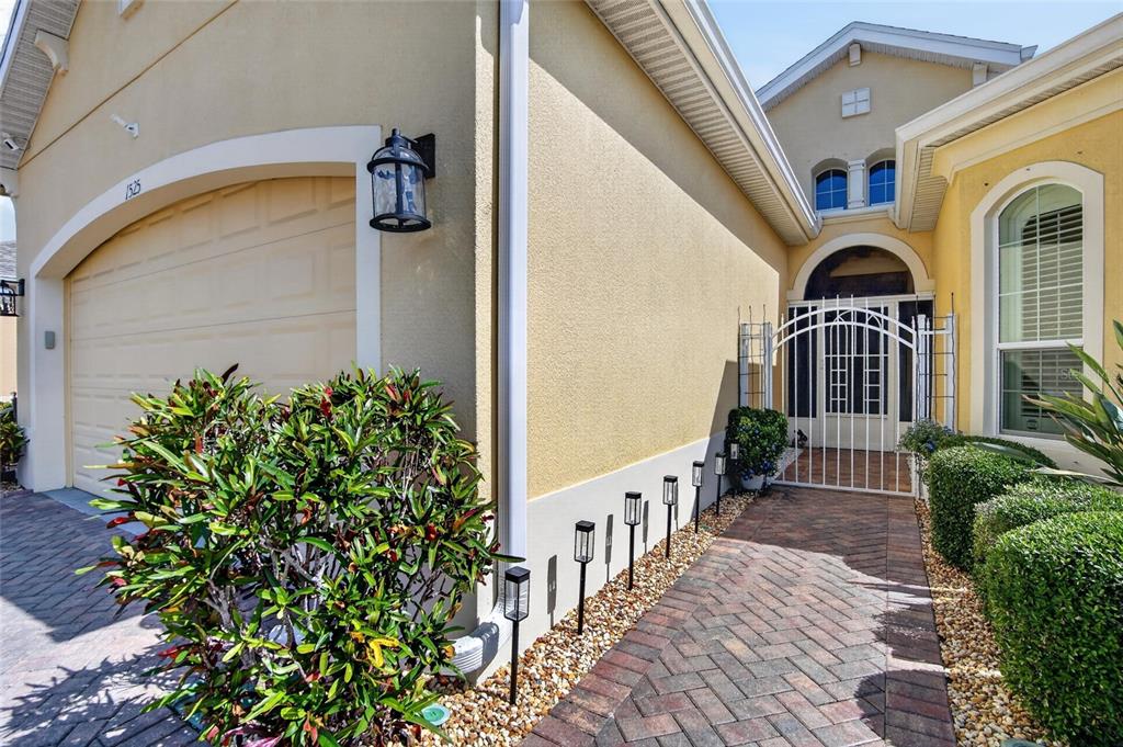 A paved walkway leads to a gated courtyard entrance beside a beige house with a garage — 1525 EMERALD DUNES DRIVE, SUN CITY CENTER, FL