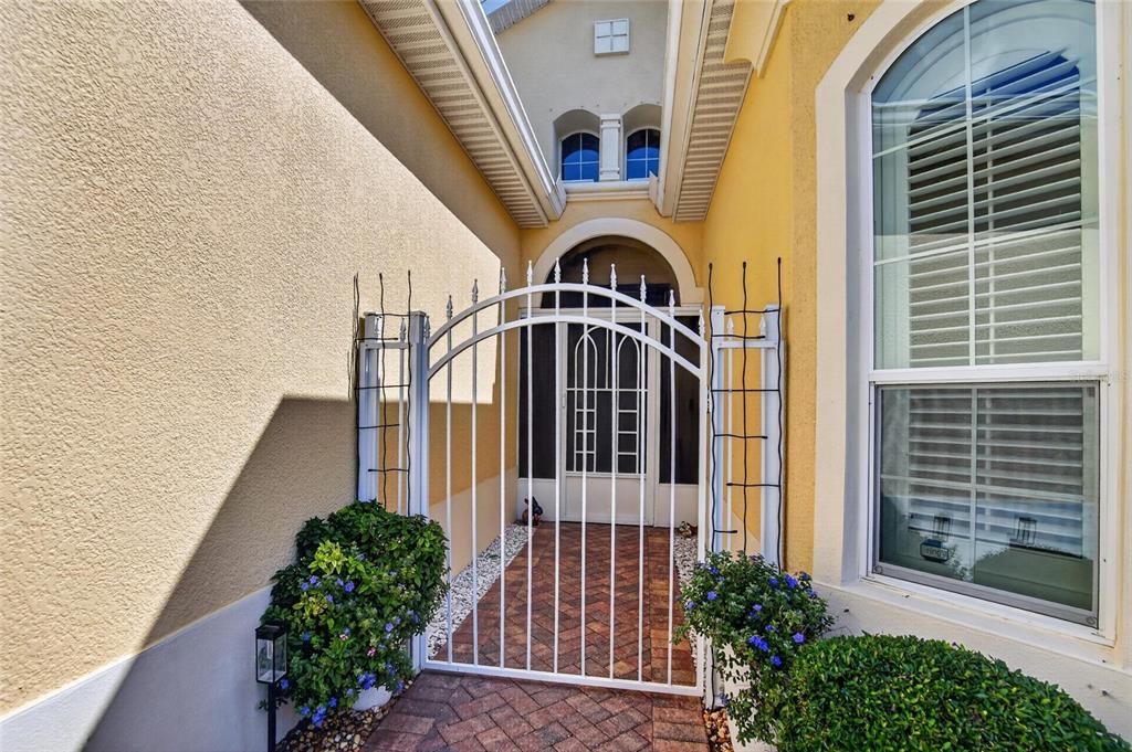 A white metal gate leads to a screened entryway with a brick walkway and yellow walls — 1525 EMERALD DUNES DRIVE, SUN CITY CENTER, FL