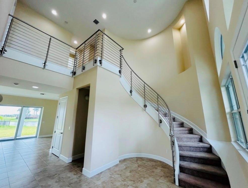 A curved staircase with a metal railing leads to an upper landing in a foyer — 5199 Liberty Lane, Westlake FL 33470, WESTLAKE, FL