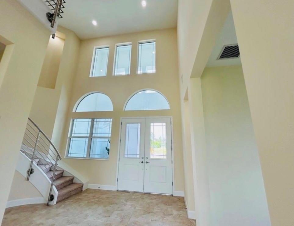 A high-ceilinged entryway features a curved staircase, double front doors, and multiple windows — 5199 Liberty Lane, Westlake FL 33470, WESTLAKE, FL