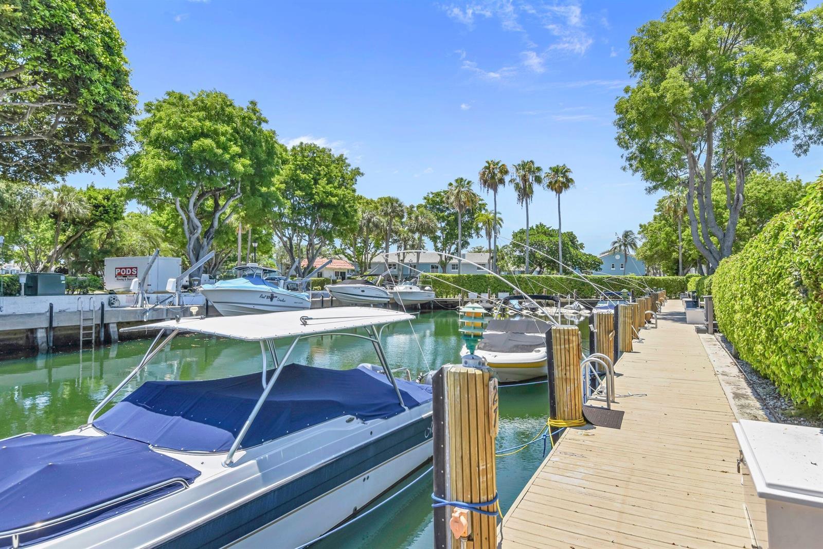 A wooden dock extends along a canal lined with boats, trees, and a green hedge — 799 Jeffery Street # 105, Boca Raton FL 33487, BOCA RATON, FL