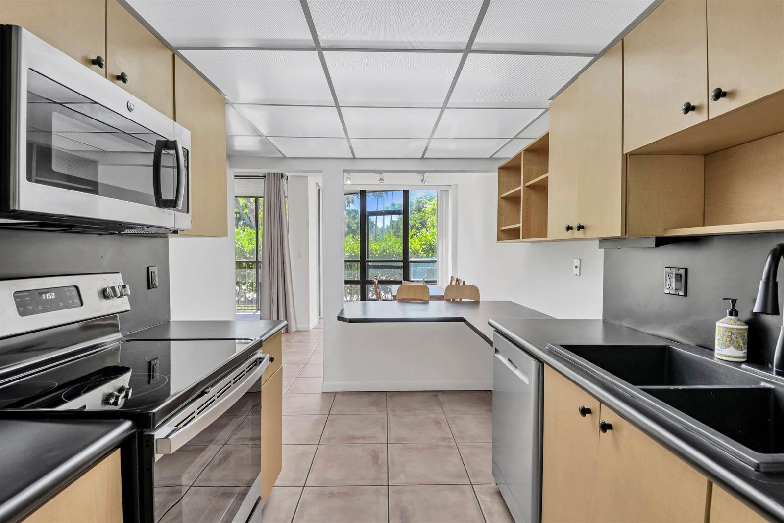 A kitchen with light wood cabinets, black countertops, and a drop ceiling overlooks a dining area — 799 Jeffery Street # 105, Boca Raton FL 33487, BOCA RATON, FL