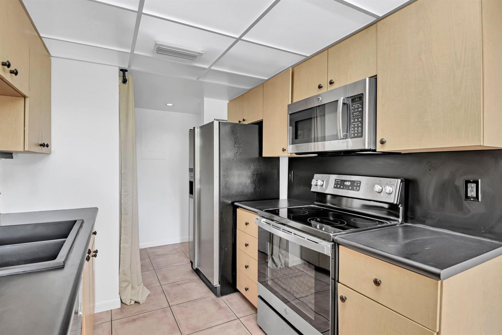 A kitchen with light wood cabinets, black countertops, stainless steel appliances, and tiled flooring — 799 Jeffery Street # 105, Boca Raton FL 33487, BOCA RATON, FL