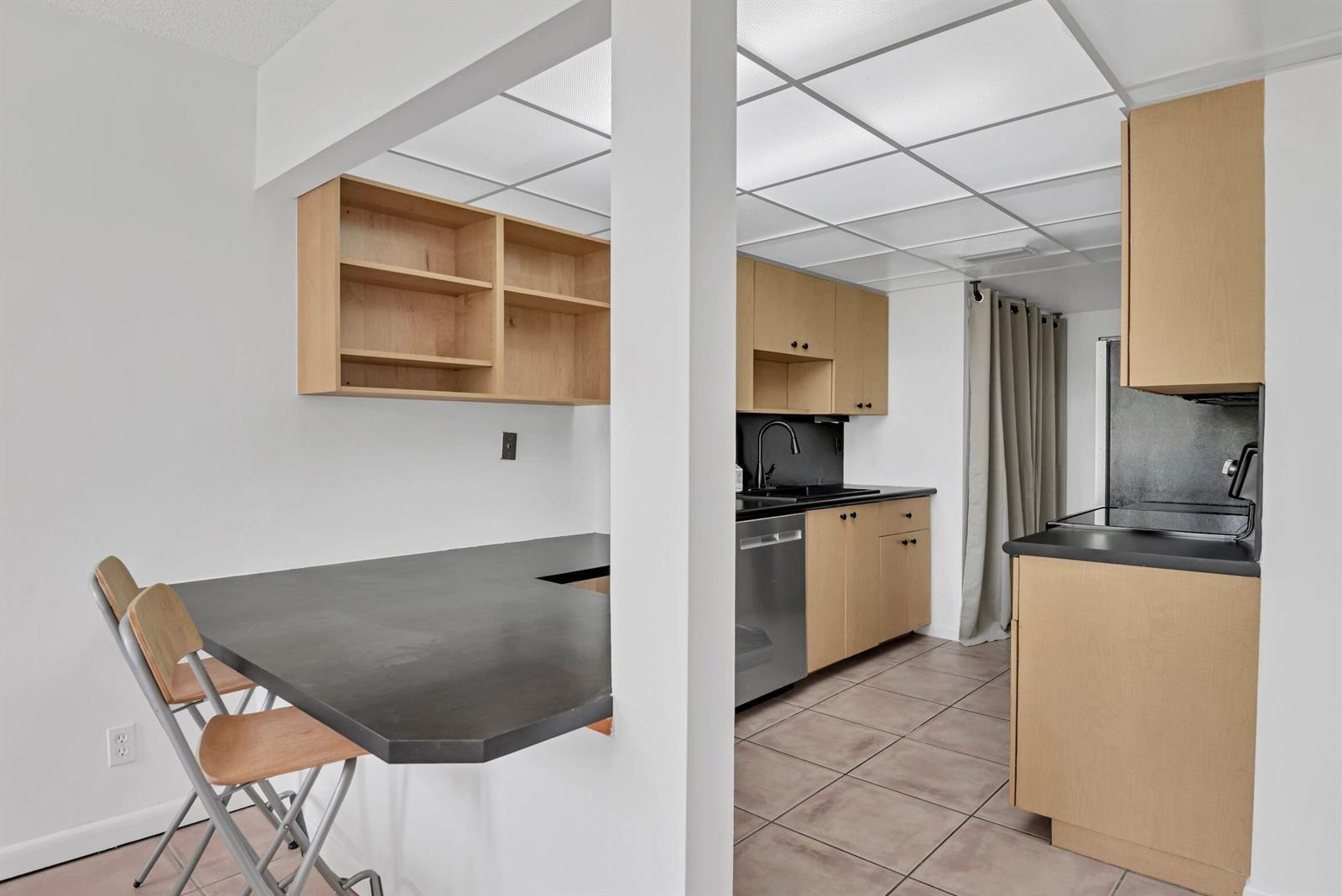 A kitchen features light wood cabinets, black countertops, tile flooring, and a breakfast bar — 799 Jeffery Street # 105, Boca Raton FL 33487, BOCA RATON, FL