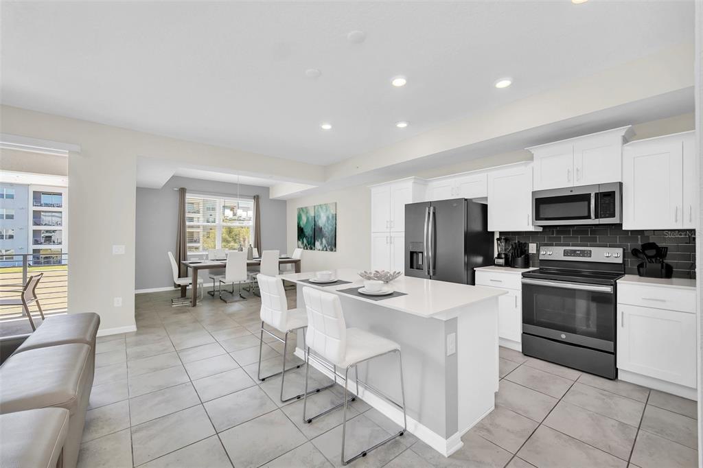 A modern kitchen with white cabinets, a central island, and an adjacent dining area — 3180 PARADOX CIRCLE UNIT 203, KISSIMMEE, FL