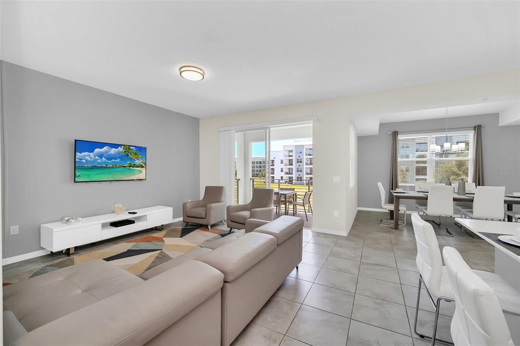 A modern living and dining area with tile floors, a sectional sofa, and a balcony — 3180 PARADOX CIRCLE UNIT 203, KISSIMMEE, FL