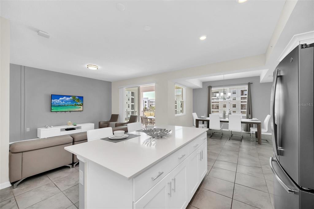 A modern kitchen island with white cabinets overlooks an open-concept living and dining area — 3180 PARADOX CIRCLE UNIT 203, KISSIMMEE, FL
