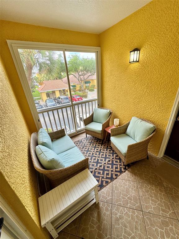 A screened-in balcony features yellow stucco walls, wicker furniture with light blue cushions, and tile — 10764 70TH AVENUE UNIT #1201, SEMINOLE, FL