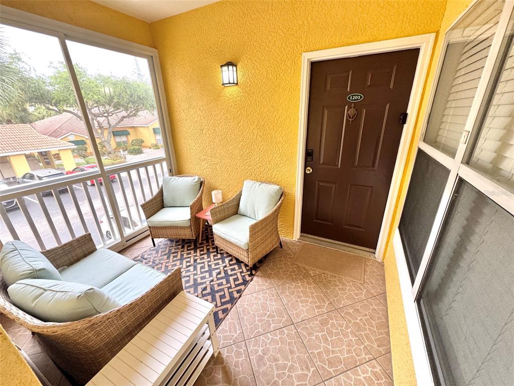 A covered balcony features wicker furniture, a patterned rug, tiled flooring, and a brown entry door — 10764 70TH AVENUE UNIT #1201, SEMINOLE, FL
