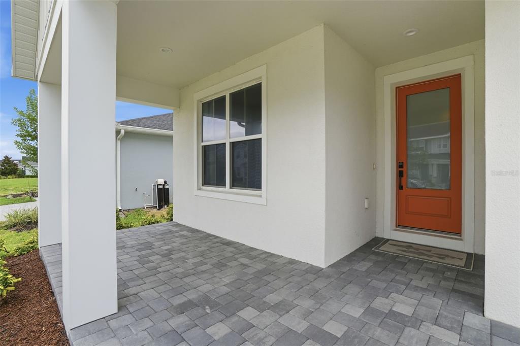 A covered front porch features gray paver flooring, a white exterior wall, and an orange door — 1658 PINECLIFF DRIVE, APOPKA, FL