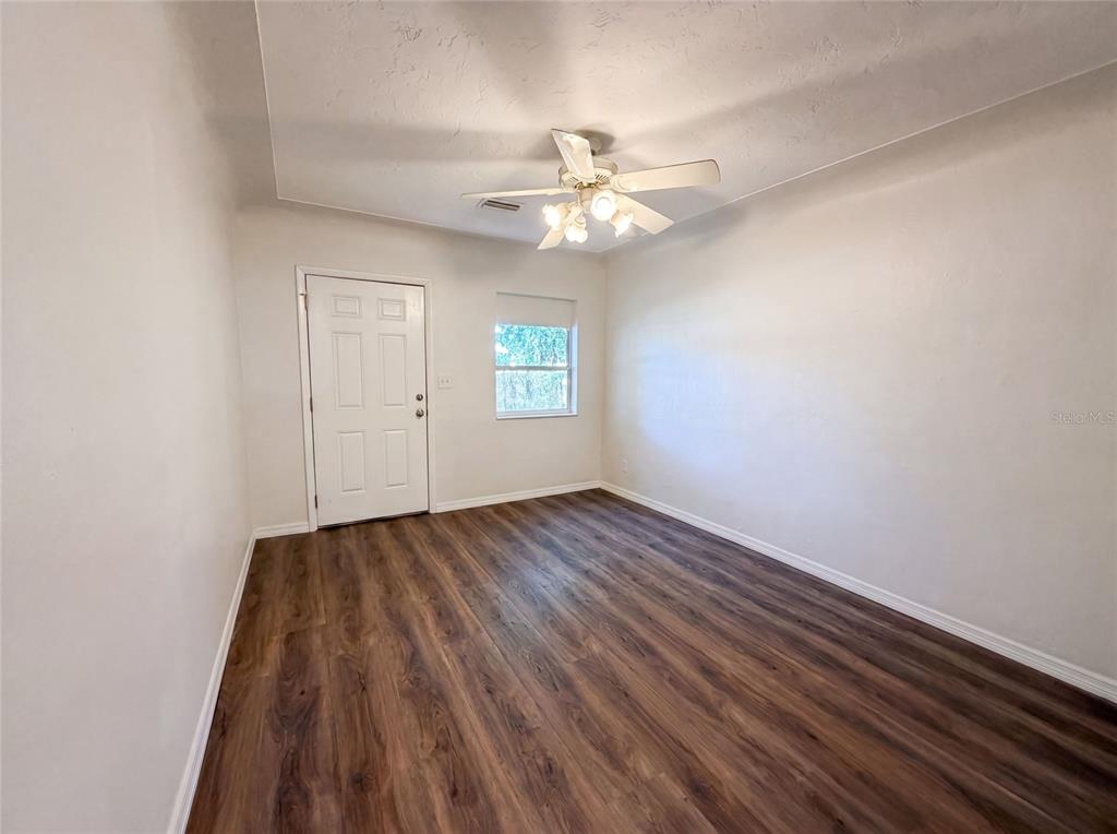 An empty room features white walls, wood-look flooring, a ceiling fan, and a single door — 2235 45TH AVENUE N, ST PETERSBURG, FL