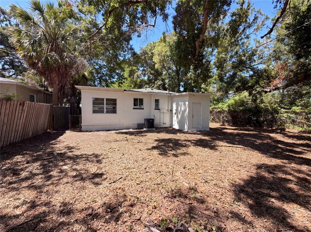 The exterior of a white, single-story house features a large, leaf-covered backyard and mature trees — 2235 45TH AVENUE N, ST PETERSBURG, FL