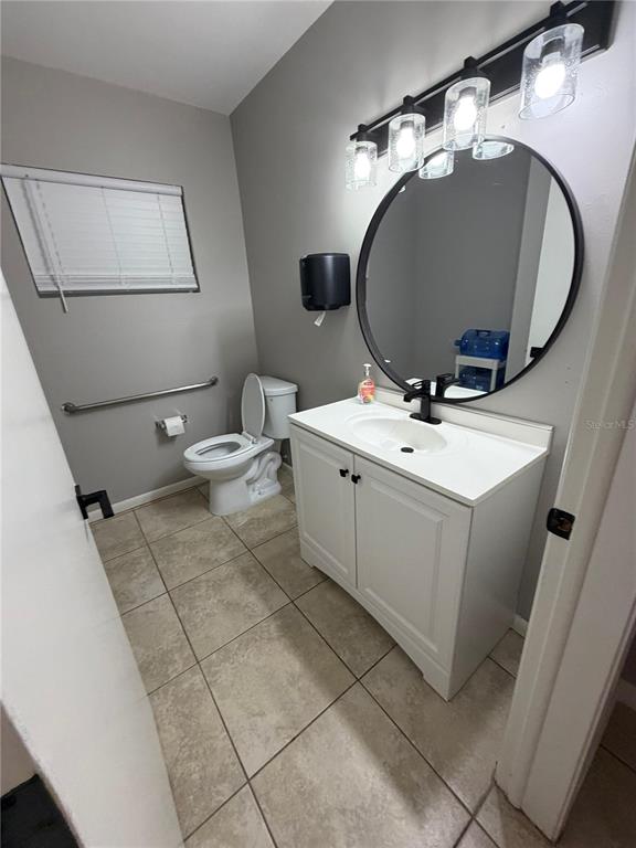 A bathroom features a white vanity, a round mirror, a toilet, and a grab bar — 5950 HIGH STREET, NEW PORT RICHEY, FL