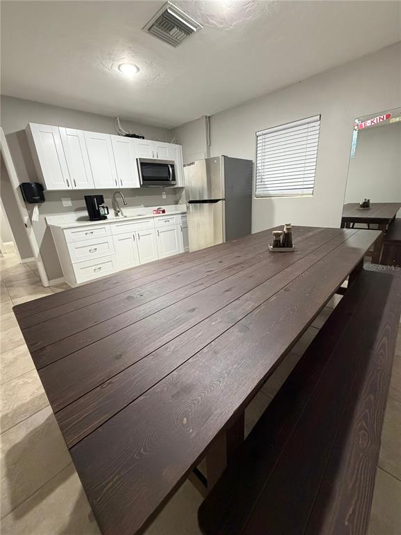 A kitchen features white cabinets, stainless steel appliances, and a large wooden dining table — 5950 HIGH STREET, NEW PORT RICHEY, FL