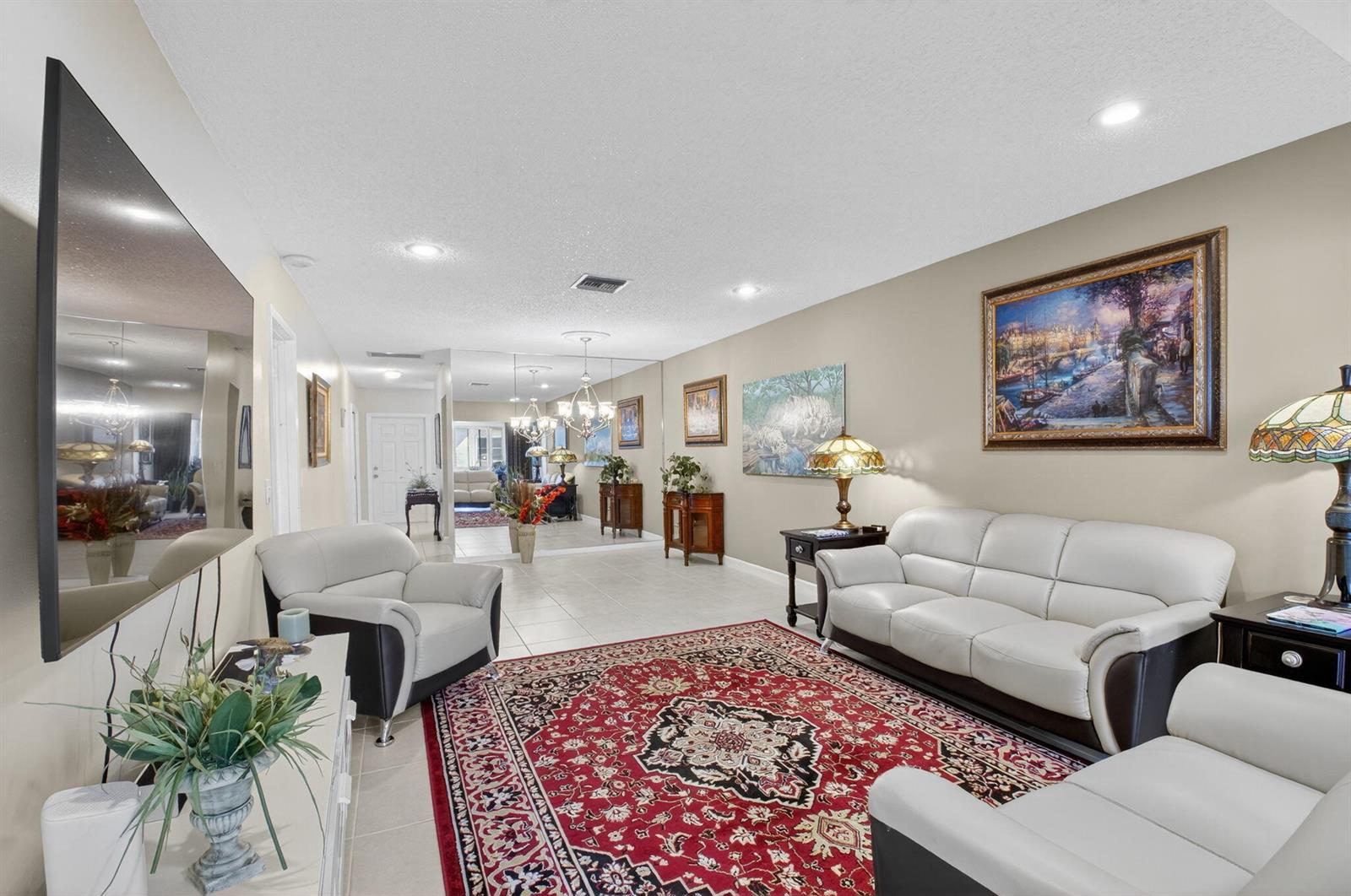 A living room features a red patterned rug, white leather furniture, and a large wall mirror — 1141 Violet Terrace # 202, Delray Beach FL 33445, DELRAY BEACH, FL