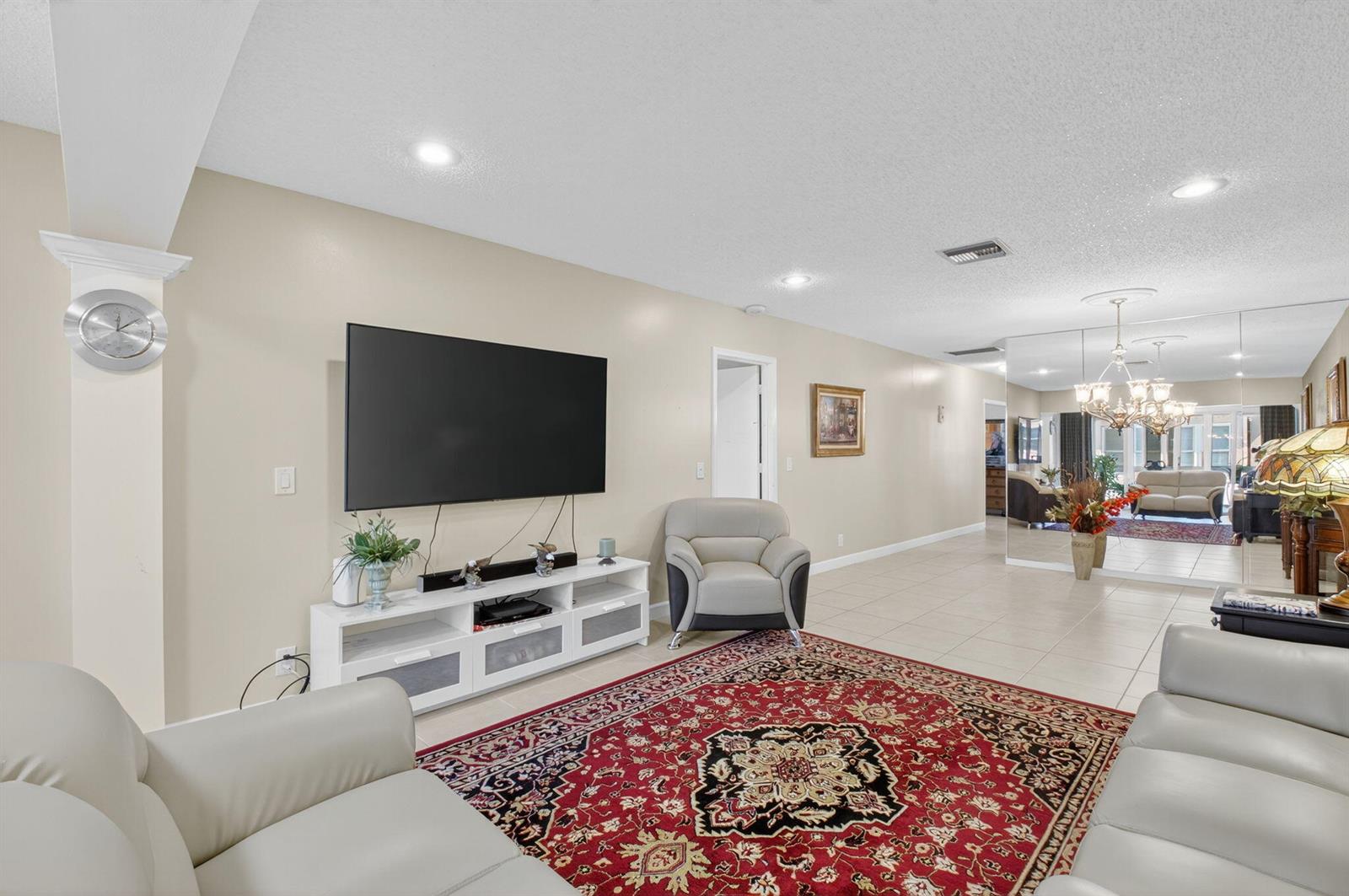A living room features a large television, white media console, leather seating, and a red rug — 1141 Violet Terrace # 202, Delray Beach FL 33445, DELRAY BEACH, FL