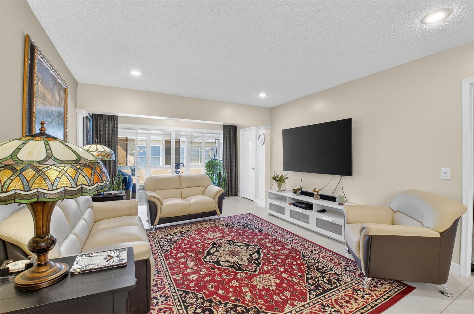 A living room features a large red patterned rug, cream leather furniture, and a wall-mounted television — 1141 Violet Terrace # 202, Delray Beach FL 33445, DELRAY BEACH, FL