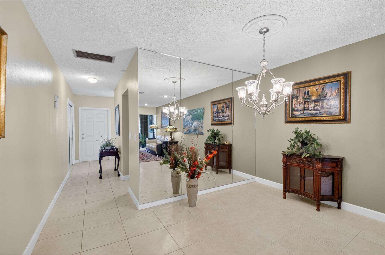 A tiled entryway features a large mirrored wall, a crystal chandelier, and a wooden cabinet — 1141 Violet Terrace # 202, Delray Beach FL 33445, DELRAY BEACH, FL
