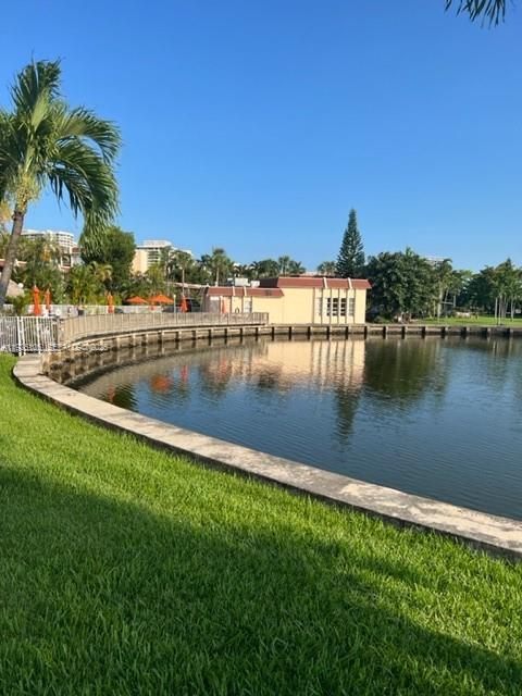 A concrete walkway borders a calm lake in front of a tan building with palm trees — 2001 Atlantic Shores Blvd # 105, Hallandale Beach FL 33009, HALLANDALE BEACH, FL