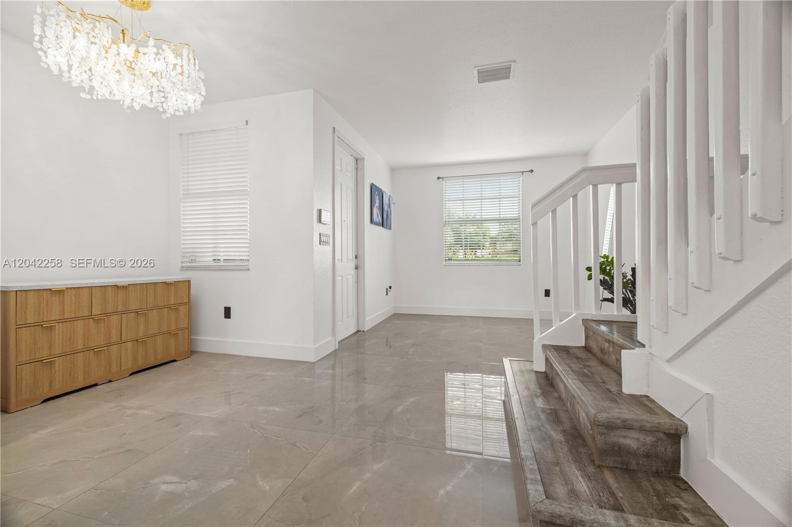 A bright entryway features large gray floor tiles, a crystal chandelier, and a wooden staircase — 3370 NE 14th Dr # 29, Homestead FL 33033, HOMESTEAD, FL