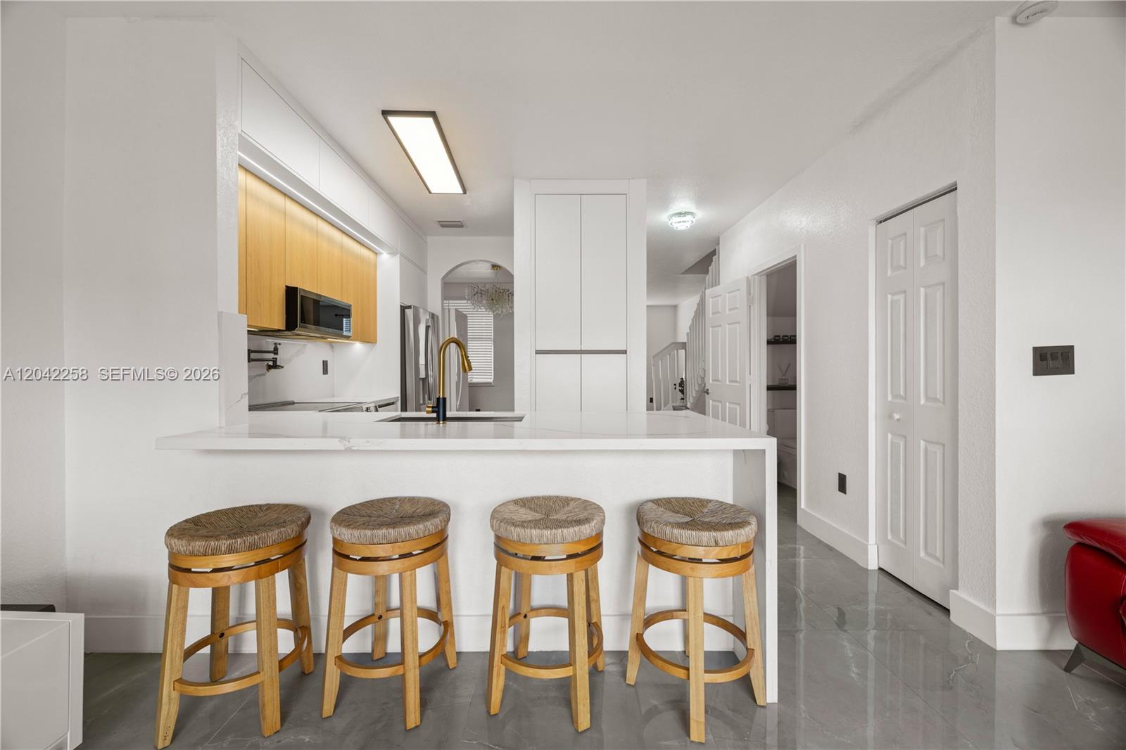 A kitchen features a white island with four wooden stools, light wood cabinets, and gray flooring — 3370 NE 14th Dr # 29, Homestead FL 33033, HOMESTEAD, FL