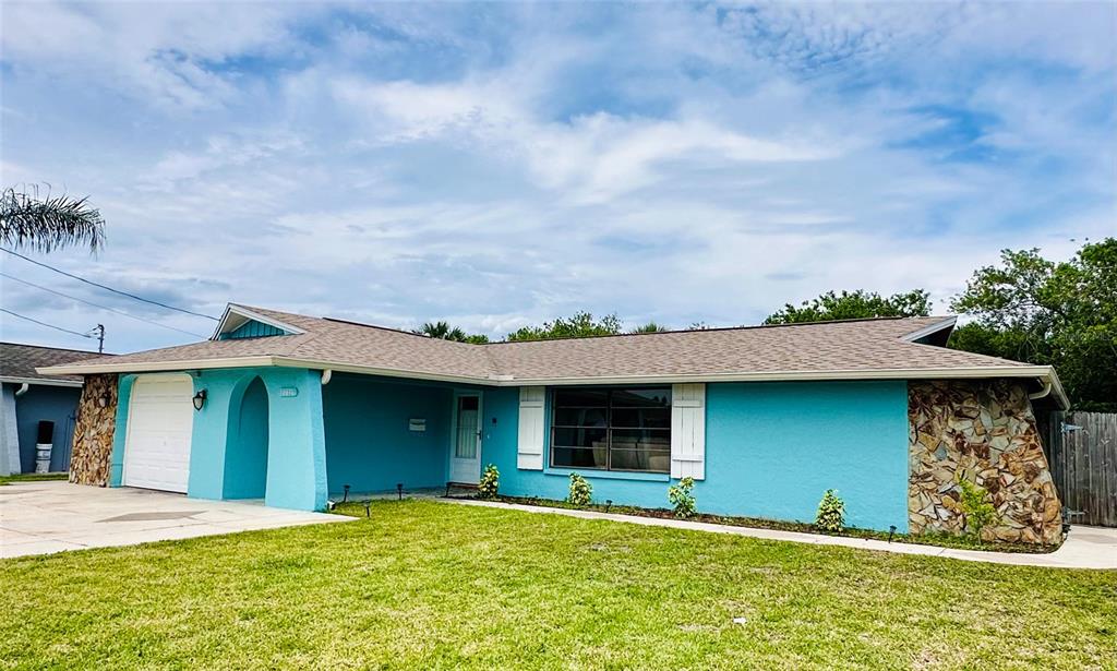 A turquoise single-story house features a stone facade, a white garage door, and a lawn — 12816 1ST ISLE, HUDSON, FL