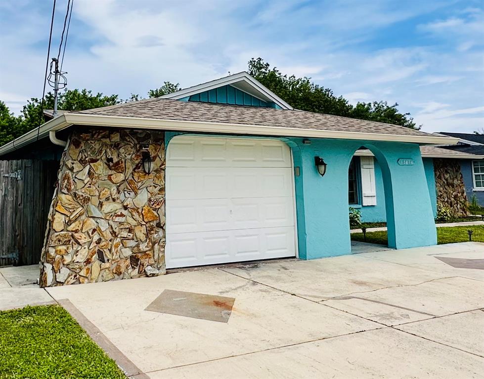 A turquoise house exterior features a white garage door, stone siding, and an arched entryway — 12816 1ST ISLE, HUDSON, FL