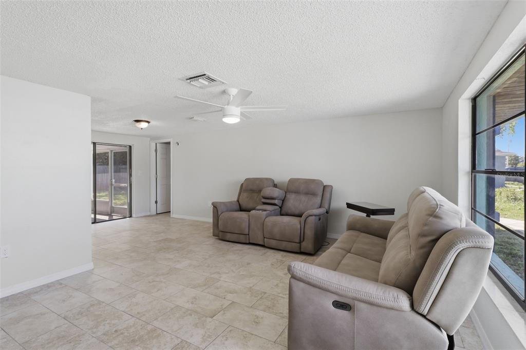 A living room with light tile flooring, two grey reclining sofas, and a ceiling fan — 12816 1ST ISLE, HUDSON, FL