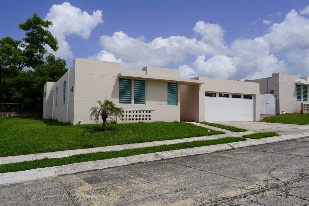 A single-story beige house with a white garage door and green louvered windows — Calle Ruisenor MIRAMELINDA ESTATES UNIT 223, RIO GRANDE, PR