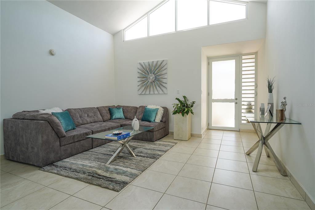 A living room features a gray sectional sofa, glass coffee table, and high vaulted windows — Calle Ruisenor MIRAMELINDA ESTATES UNIT 223, RIO GRANDE, PR