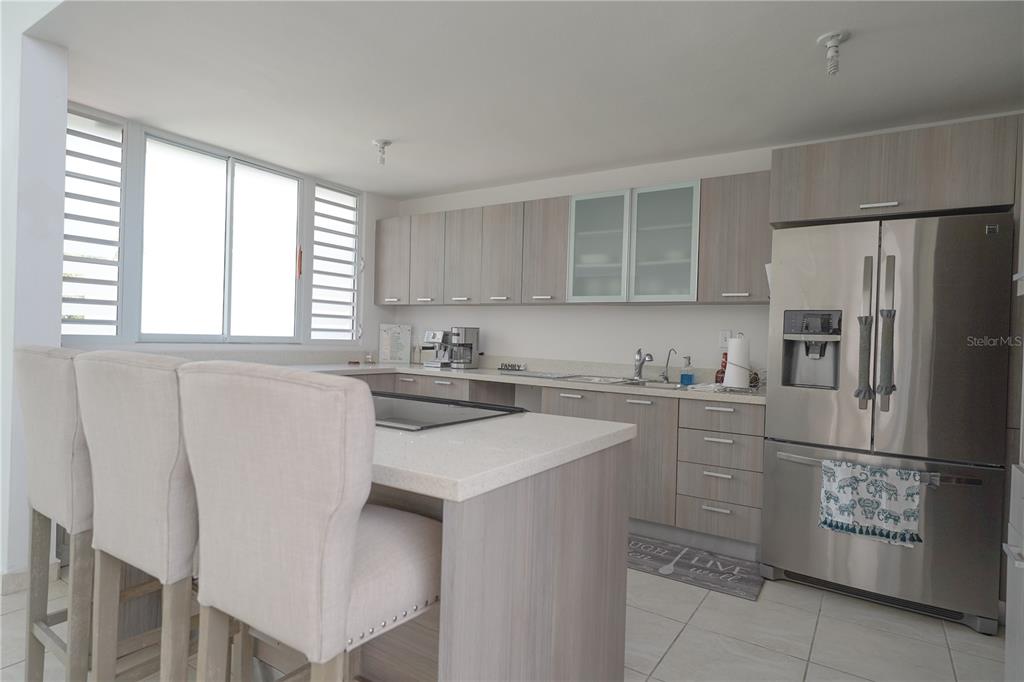A kitchen features light wood cabinetry, a central island with seating, and stainless steel appliances — Calle Ruisenor MIRAMELINDA ESTATES UNIT 223, RIO GRANDE, PR