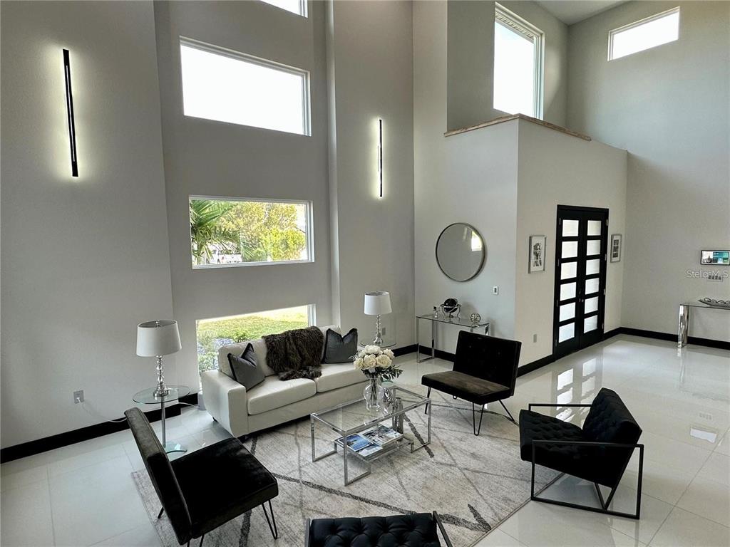 A modern living room features high ceilings, large windows, white tile floors, and black furniture — 6524 6TH AVENUE N, ST PETERSBURG, FL