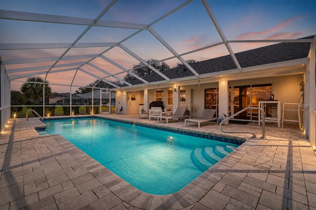 A screened-in swimming pool with a paver deck and lounge chairs at sunset — 11009 WOODLAND WATERS BOULEVARD, WEEKI WACHEE, FL