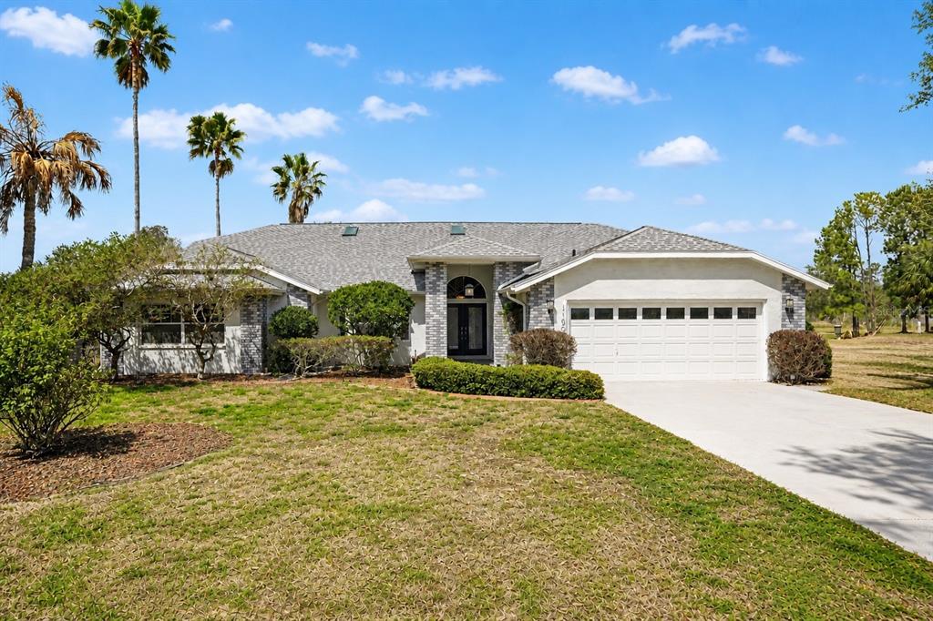 A single-story house with a gray shingled roof, brick accents, and a two-car garage — 11009 WOODLAND WATERS BOULEVARD, WEEKI WACHEE, FL