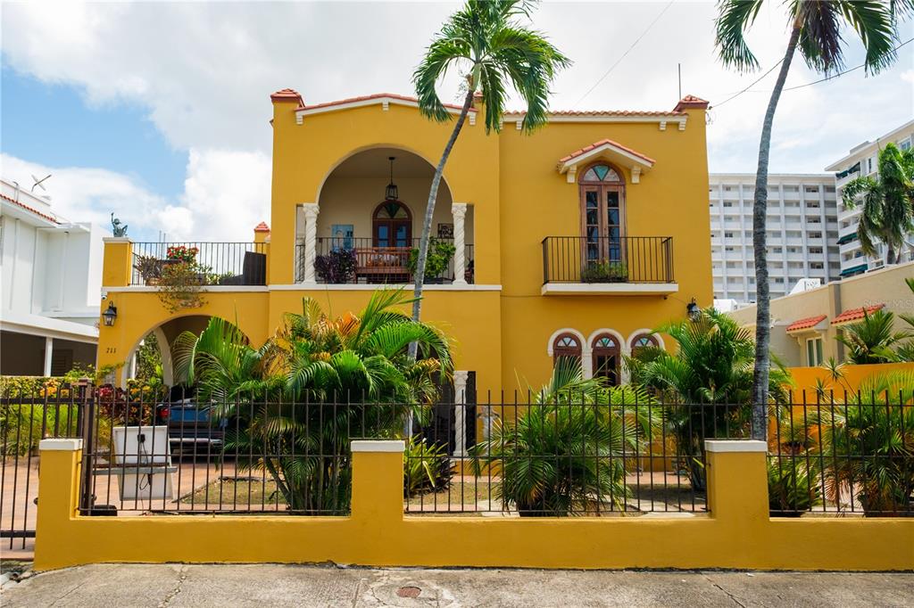 A two-story yellow stucco house with arched balconies and a metal fence in front — 711 CONCORDIA ST., MIRAMAR DEV., SAN JUAN, PR