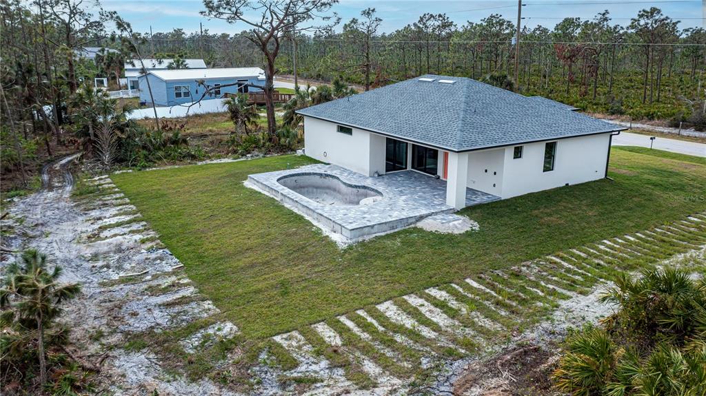 An aerial view shows a modern house with a pool and patio in a wooded area — 22528 MINERVA AVENUE, PORT CHARLOTTE, FL