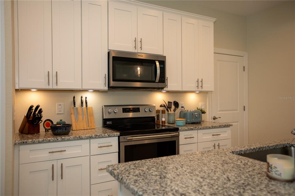 A kitchen features white cabinets, granite countertops, stainless steel appliances, and under-cabinet lighting — 22528 MINERVA AVENUE, PORT CHARLOTTE, FL