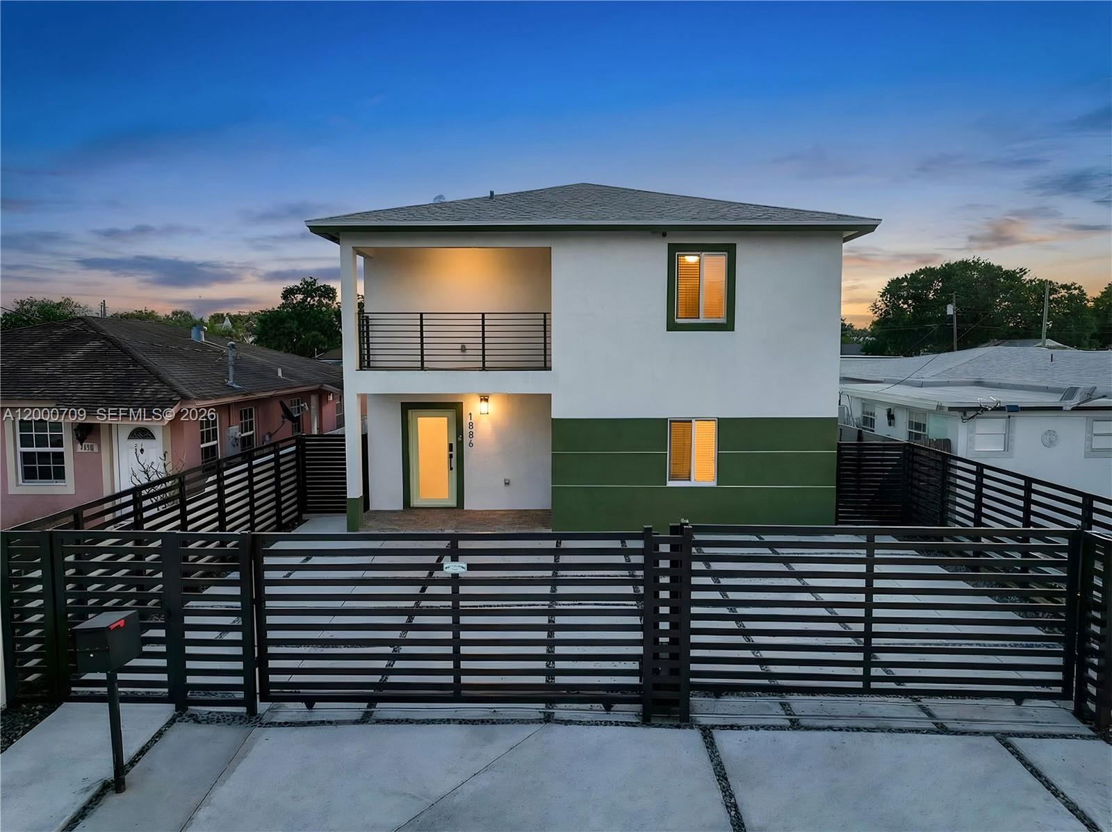 A two-story house with a green and white exterior features a balcony and gated driveway — 1886 NW 68th St, Miami FL 33147, MIAMI, FL