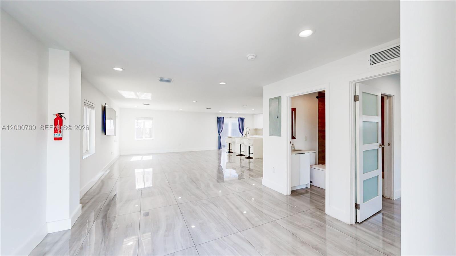 A bright, open-concept living area features white walls, glossy tile flooring, and a kitchen island — 1886 NW 68th St, Miami FL 33147, MIAMI, FL