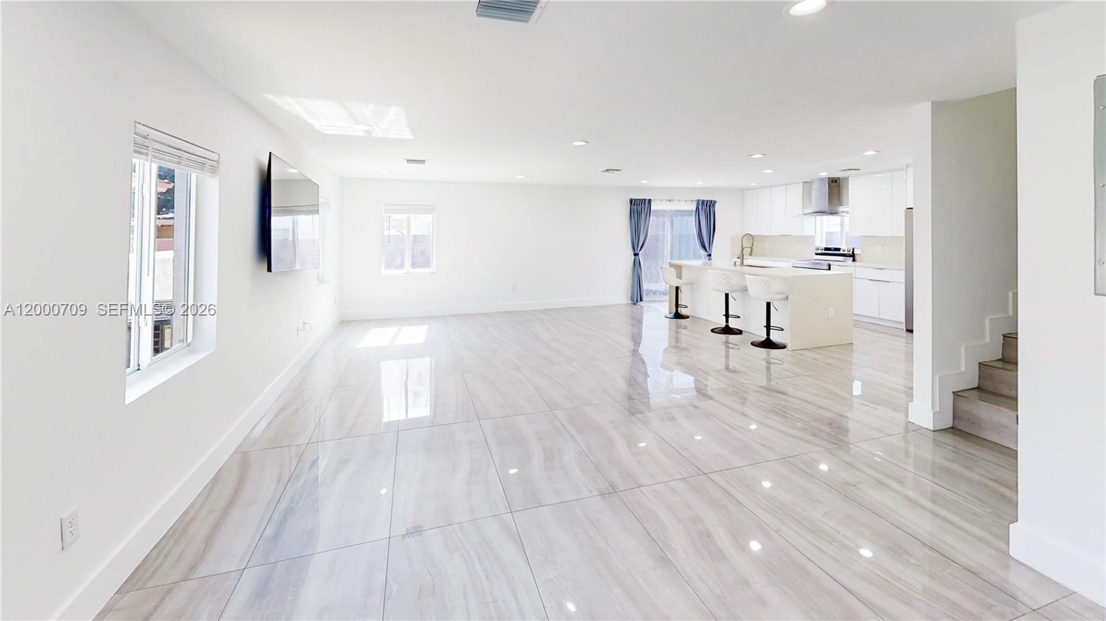 An open-concept living area features glossy tile floors, a kitchen island, and a staircase — 1886 NW 68th St, Miami FL 33147, MIAMI, FL
