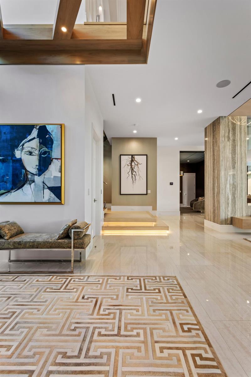 A modern foyer features a patterned rug, a bench, abstract art, and illuminated wooden steps — 4111 Ibis Point Circle, Boca Raton FL 33431, BOCA RATON, FL