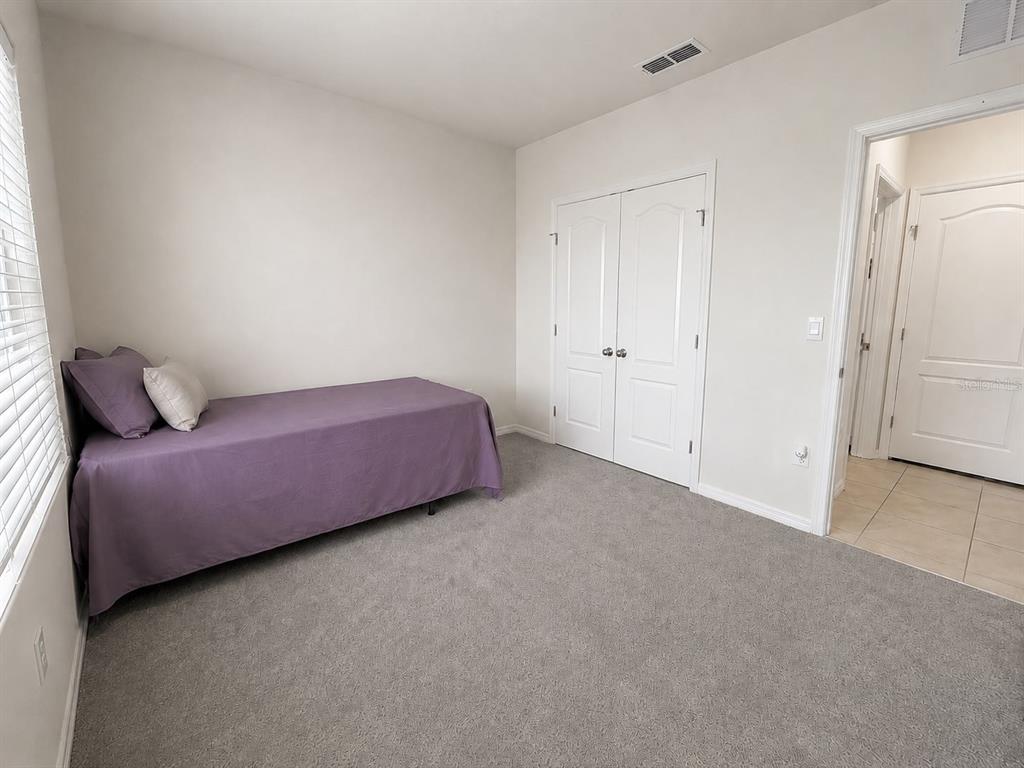 A bedroom features gray carpeting, a single bed with purple bedding, and white closet doors — 1117 GRIFFON AVENUE, LAKE ALFRED, FL