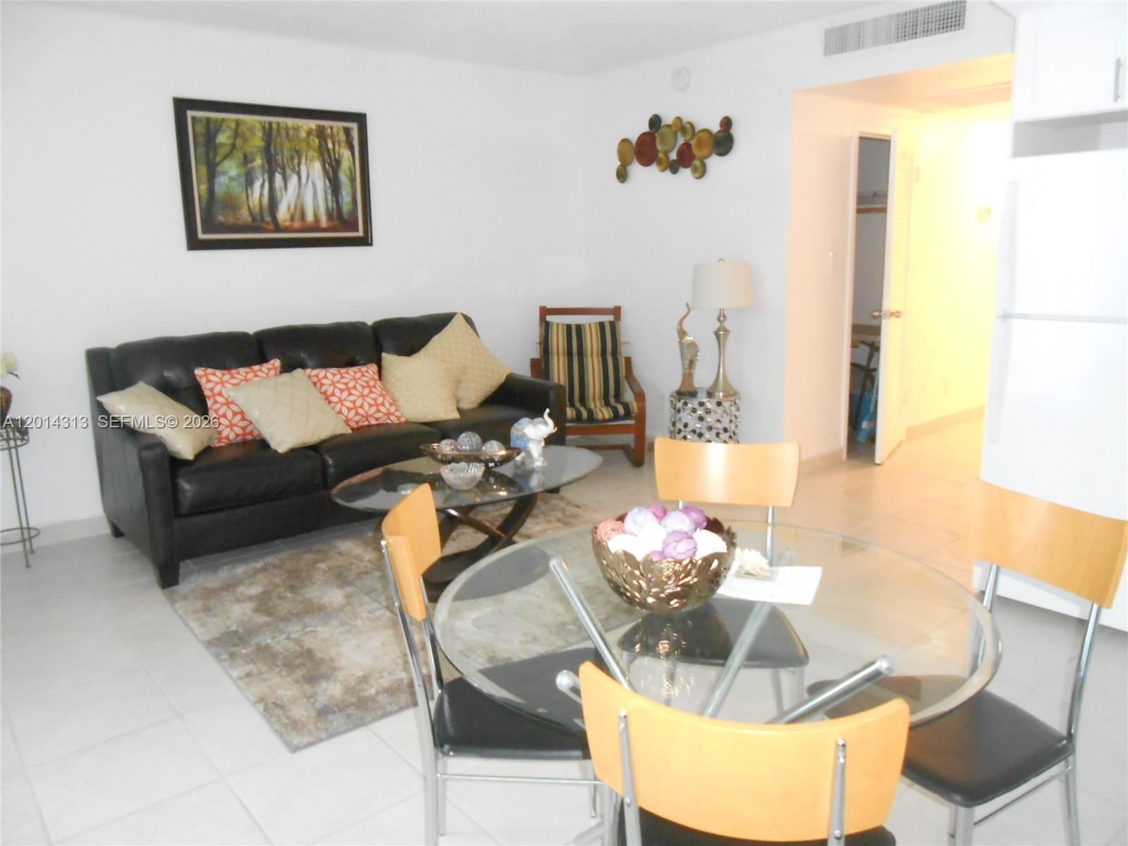 A living and dining area features a black leather sofa, glass tables, and tile flooring — 5401 Collins Ave # 932, Miami Beach FL 33140, MIAMI BEACH, FL