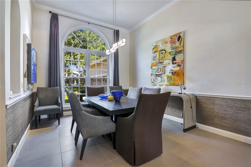 A dining room features a dark table, upholstered chairs, a large arched window, and artwork — 11462 CLAYMONT CIRCLE, WINDERMERE, FL