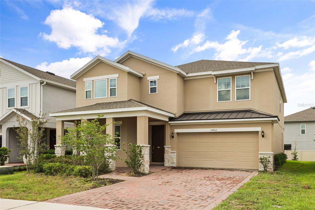 A two-story tan house with a brick driveway, stone-accented columns, and a two-car garage — 14452 CRESTAVISTA AVENUE, CLERMONT, FL