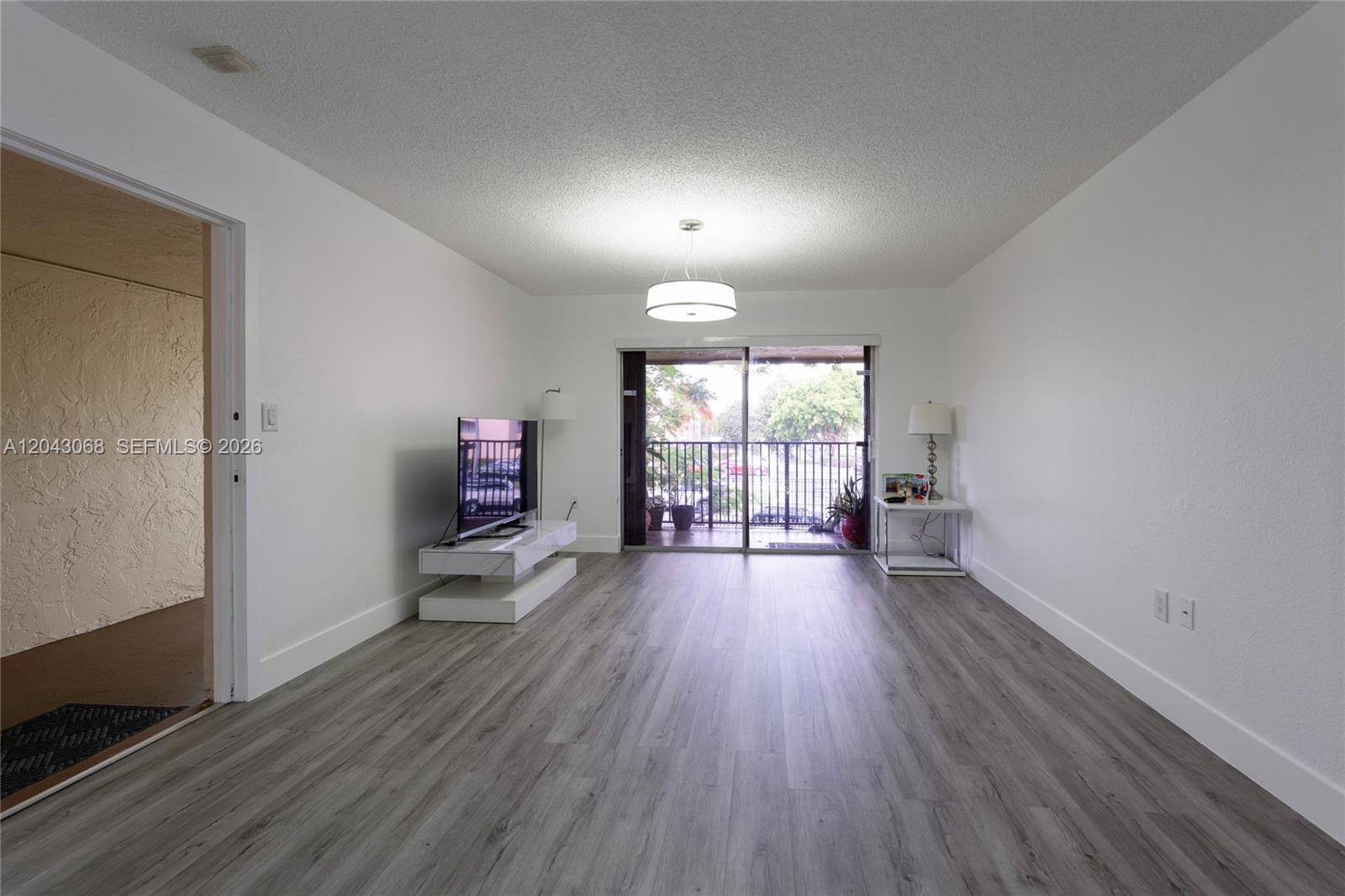 A living room features gray wood-look flooring, white walls, a sliding glass door, and a balcony — 10501 SW 108th Ave # 209, Miami FL 33176, MIAMI, FL
