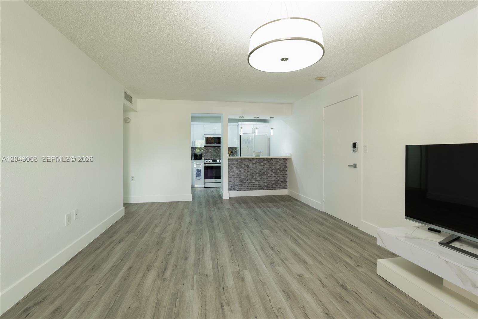 A living room with light wood-look flooring leads to a kitchen with a brick-faced bar — 10501 SW 108th Ave # 209, Miami FL 33176, MIAMI, FL