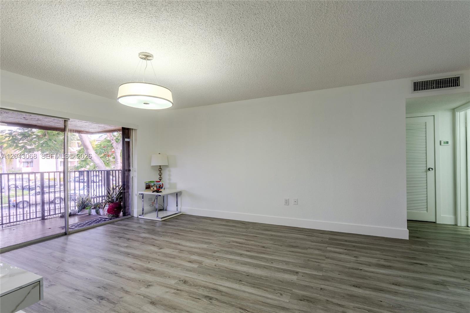 An empty living room features wood-look flooring, a modern pendant light, and a sliding glass door — 10501 SW 108th Ave # 209, Miami FL 33176, MIAMI, FL