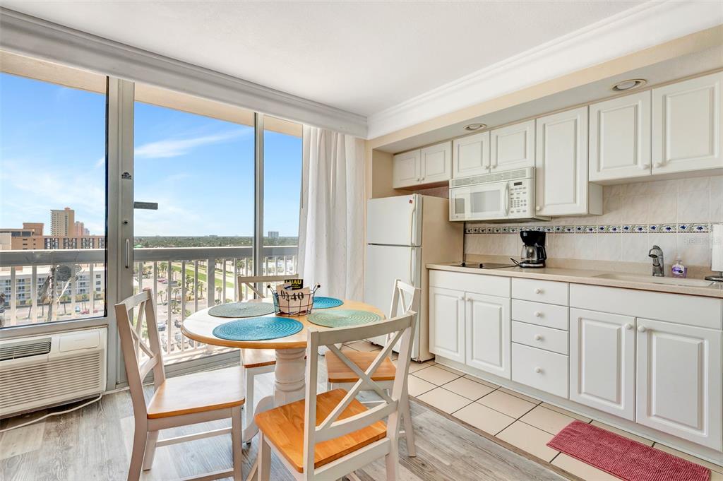 A kitchen and dining area feature white cabinets, a round table, and a balcony view — 2700 N ATLANTIC AVENUE UNIT 1006, DAYTONA BEACH, FL