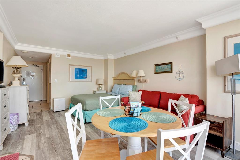 A studio apartment features a bed, a red sofa, and a round dining table — 2700 N ATLANTIC AVENUE UNIT 1006, DAYTONA BEACH, FL